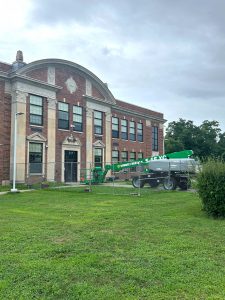 An exterior view of Van Schaick Elementary School with a green construction lift in the foreground.