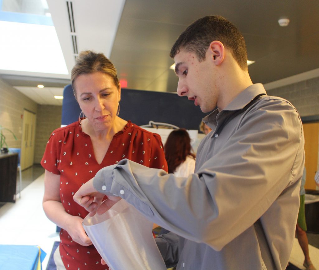 A high school student explains a science project to an attentive adult.