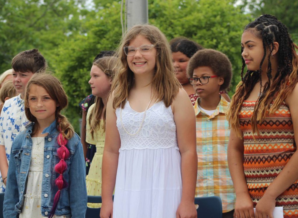 Several middle school students wait during an award ceremony outdoors.