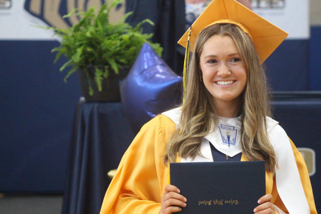 A graduate clutches her diploma and smiles proudly.