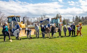 Several people in hardhats break the ground with shovels.