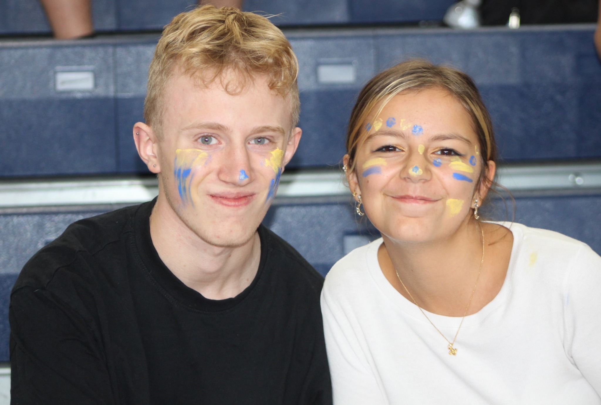 Two high school students pose together with blue and yellow face paint.