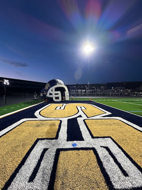 A closeup of the turf field's ground with a football helmet and spotlight overhead.