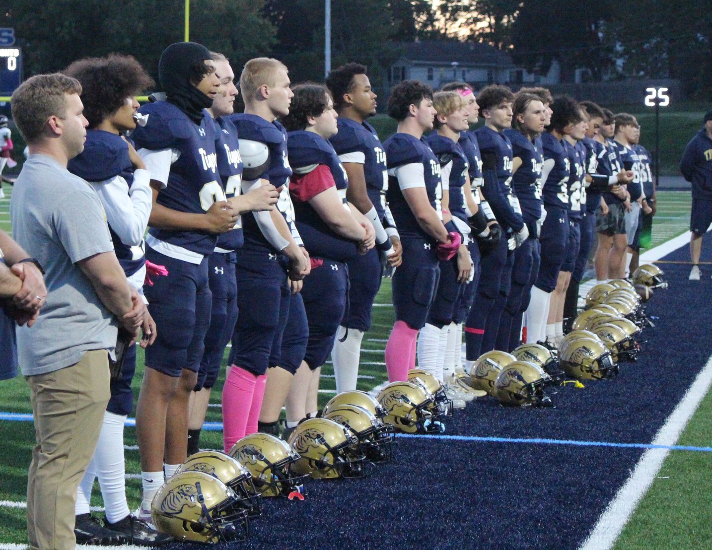 High school football players stand in a line with helmets on the ground.