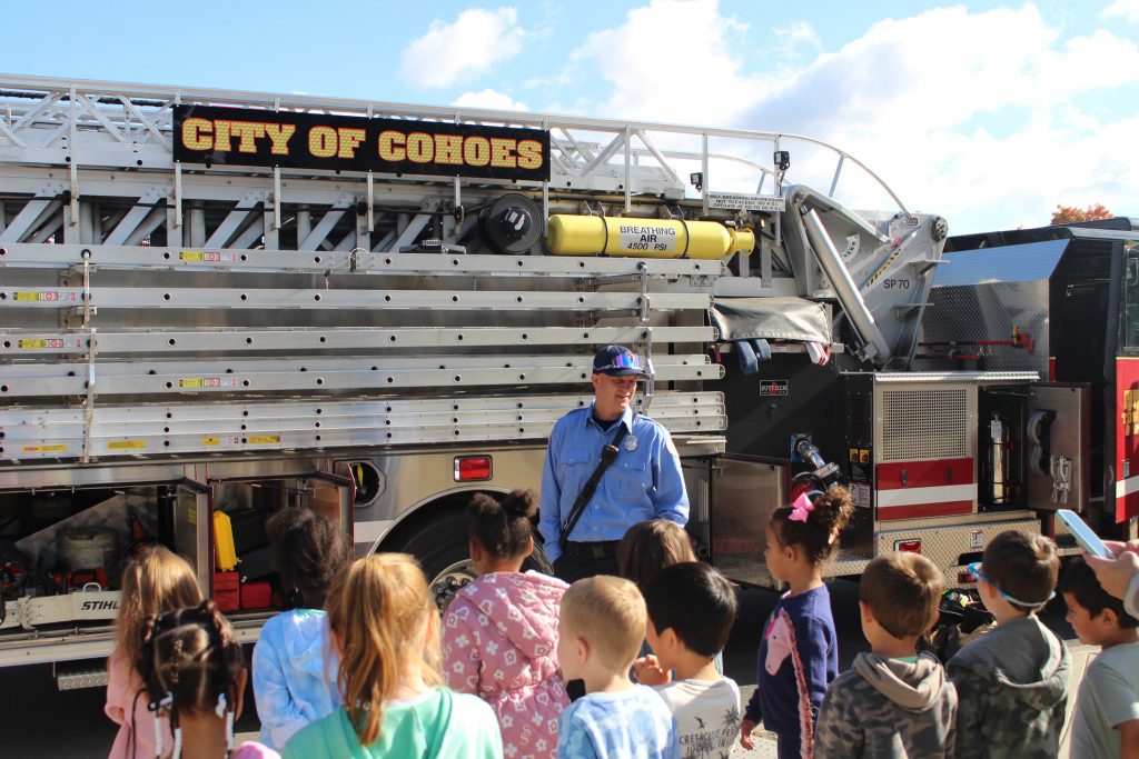 A Cohoes firefighter talks with a group of young students in front of a fire truck.