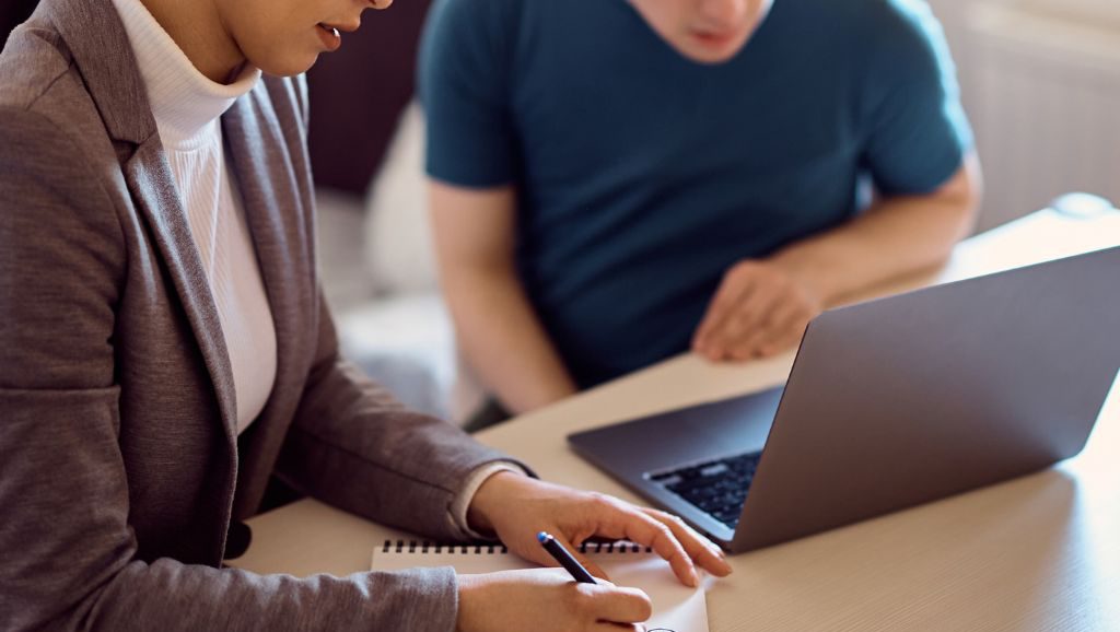 A middle school student examines a laptop screen while a counselor takes notes.