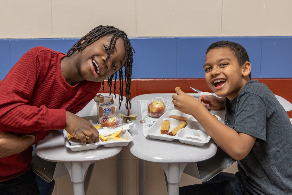 two students smile while eating lunch together