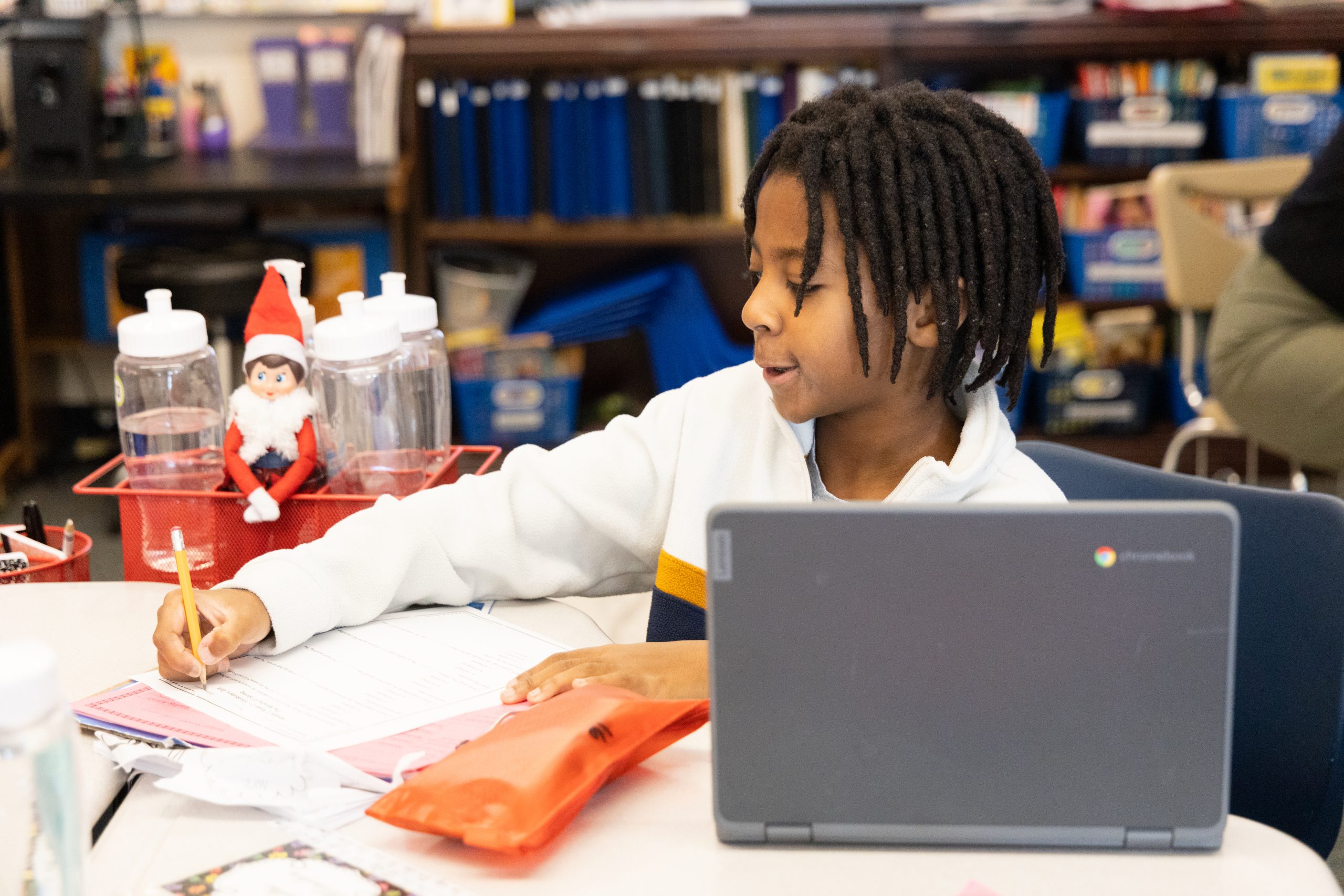 van schaick elementary student works on chromebook in class while writing on paper