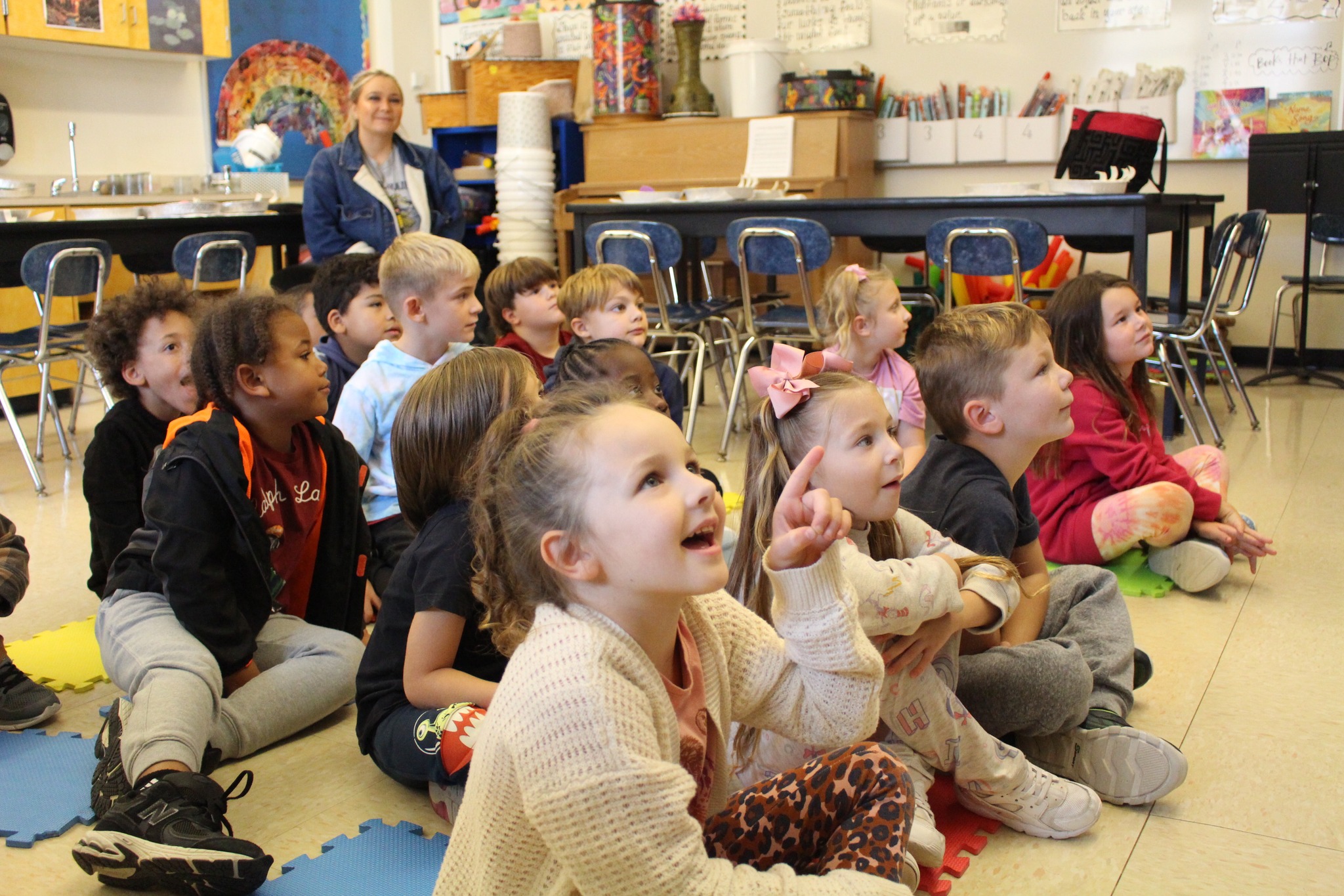 Several elementary students sit on the floor listening to a story.