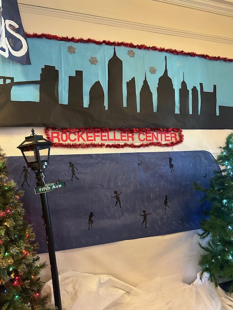 A craft paper version of Rockefeller Center on a wall with cutout ice skating people.